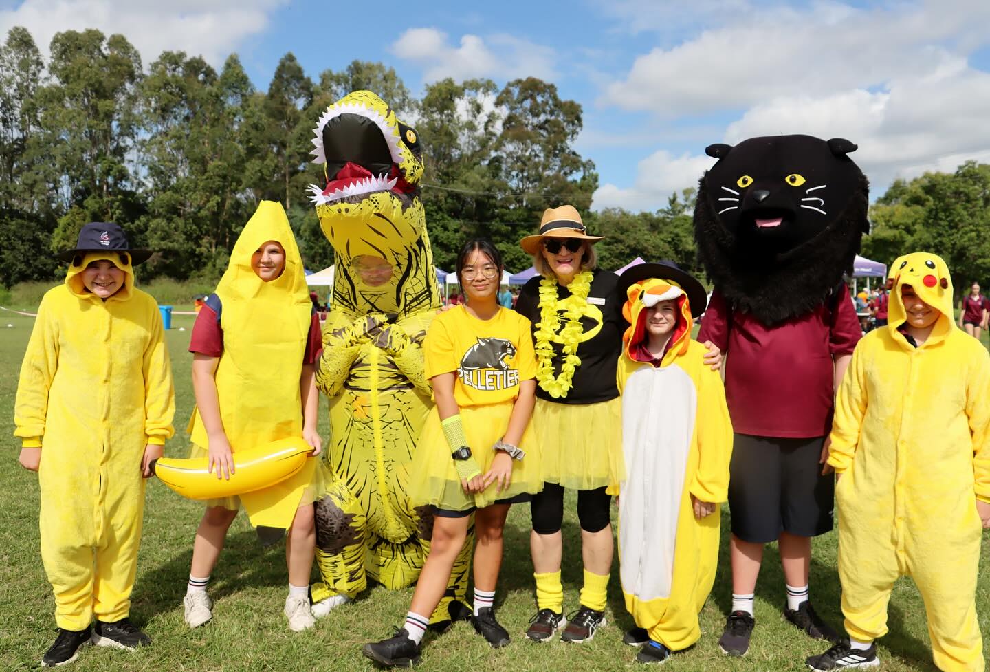 Group of students dressed in themed costumes standing together on a grassy field during a school event.