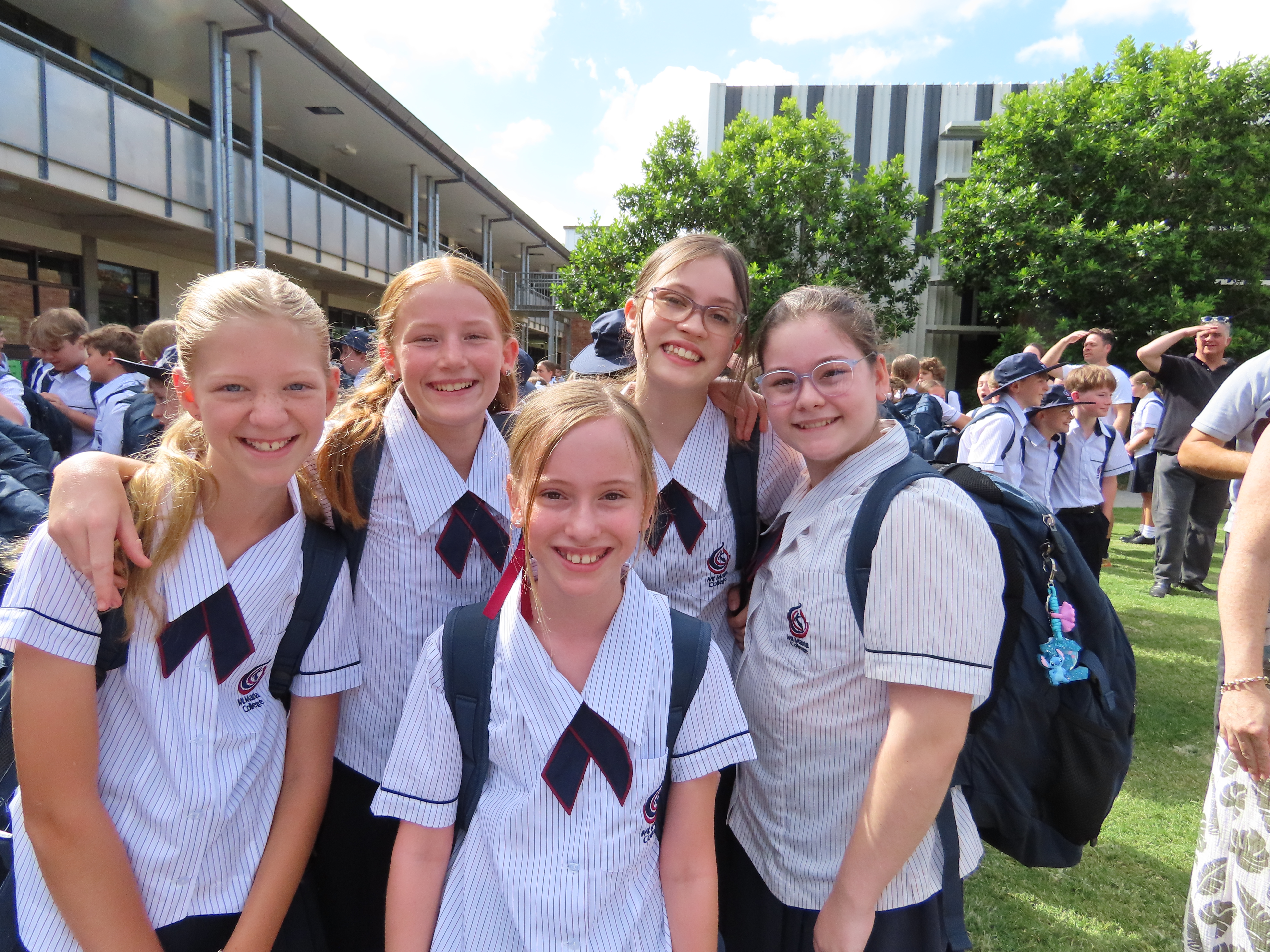Group of students in school uniform standing together outdoors on campus, smiling for the camera.