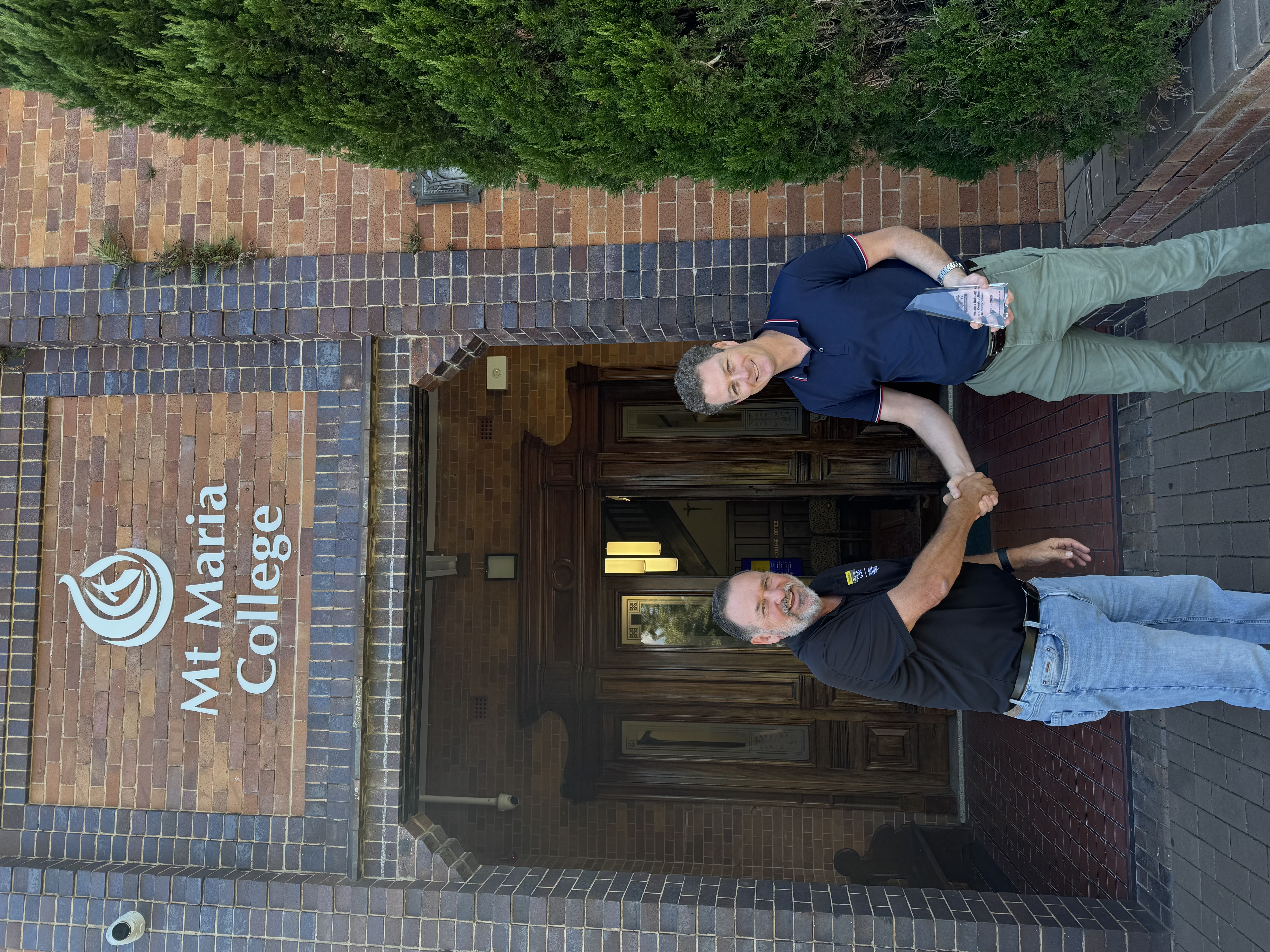 Two adults shake hands outside the entrance of Mt Maria College.